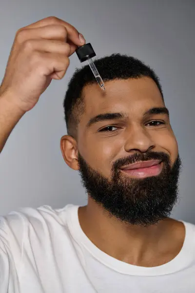 African american good looking young man with a beard holding a bottle of serum. — Stock Photo