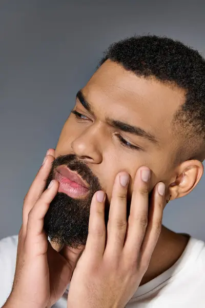 Handsome young man in white t-shirt tending to his beard. — Stock Photo