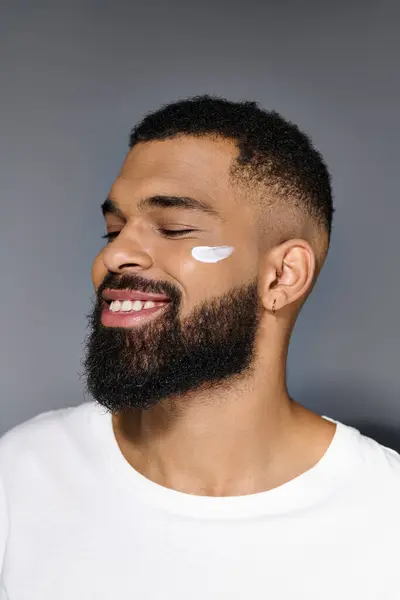 Africano americano bonito homem com uma barba mostrando creme branco em seu rosto. — Fotografia de Stock