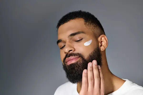 Jeune homme afro-américain avec une barbe présentant de la crème blanche sur son visage. — Photo de stock