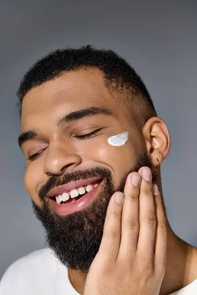 Afro-américain séduisant homme avec une barbe mettant en valeur la crème blanche sur son visage. — Photo de stock