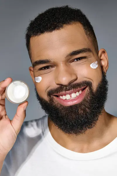 Handsome young man with a beard holding a jar of cream. — Stock Photo