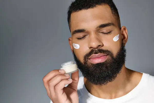A handsome young man with a beard applying cream to his face. — Stock Photo