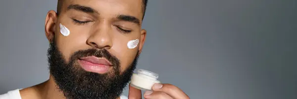 Africain américain beau jeune homme qui applique de la crème sur son visage. — Photo de stock