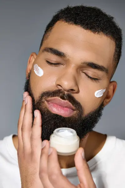 Beau homme avec une barbe tenant un pot de crème pour sa routine de soins de la peau. — Photo de stock