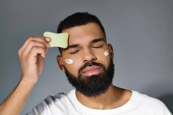 African american stylish man with cream on his face using face roller. — Stock Photo