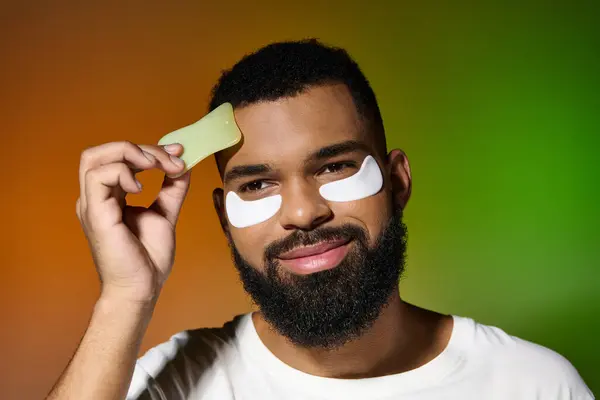 A man with a beard and eye patches on his face, engaging in skin care routine. — Stock Photo