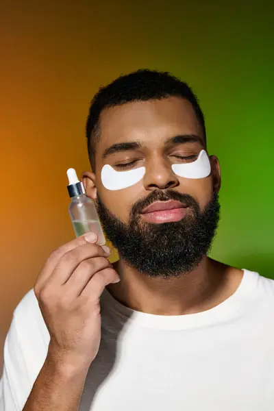 Handsome young man with beard applying eye patches for skincare routine. — Stock Photo