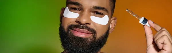 Homme barbu afro-américain utilisant des patchs oculaires et du sérum. — Photo de stock