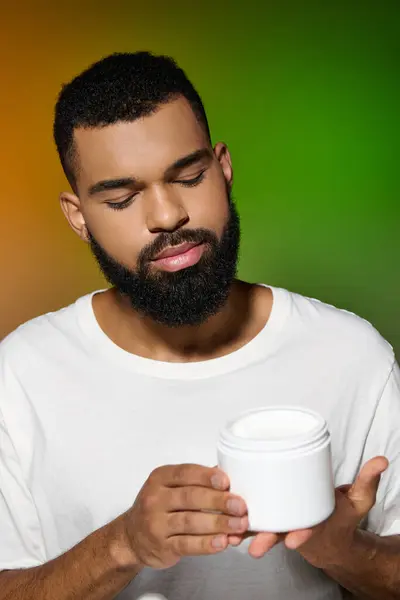 African american handsome man with a beard holds jar of cream. — Stock Photo