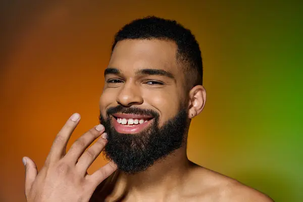 Un jeune homme souriant avec une barbe montrant sa routine de soins de la peau. — Photo de stock