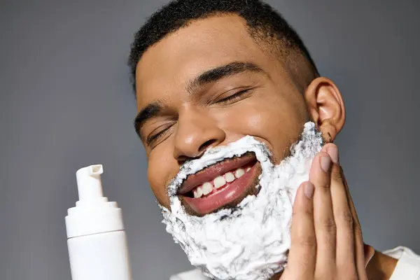 A young man in the midst of his skin care routine, shaving his face with a layer of foam. — Stock Photo