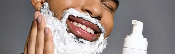 Ein schöner junger Mann rasiert sich sein Gesicht mit Schaum. — Stockfoto