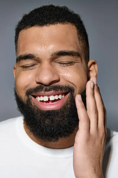 Hombre guapo con barba sonríe mientras toca su cara. - foto de stock
