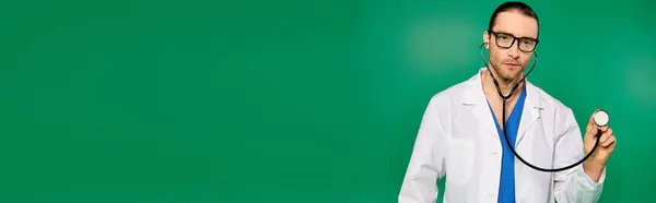 Handsome doctor in white robe with stethoscope on green backdrop. — Stock Photo