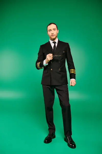 Um belo piloto masculino em um uniforme preto bate uma pose contra um cenário verde vibrante. — Fotografia de Stock