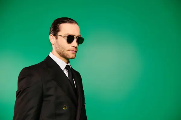 Handsome pilot in black suit and sunglasses striking a pose against a vibrant green background. — Stock Photo