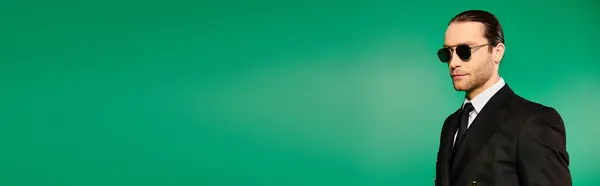 Handsome male pilot in black suit and sunglasses standing confidently against a vivid green backdrop. — Stock Photo