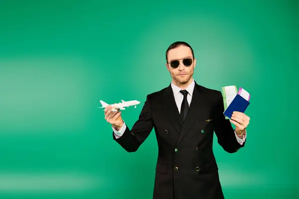Handsome pilot in black suit poses with tickets and passport and model airplane. - foto de stock