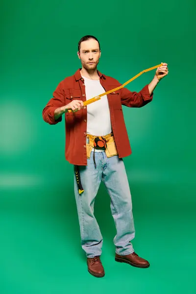 Un hombre con una chaqueta roja sostiene una cinta métrica sobre un fondo verde. - foto de stock