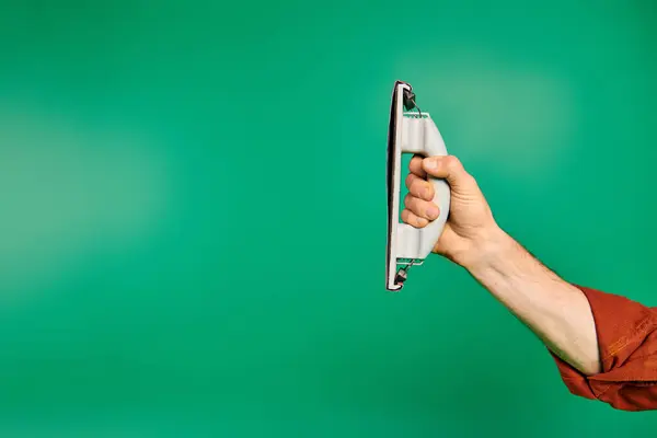 Una mano enfocada, sosteniendo un pulidor sobre un vibrante fondo verde. - foto de stock