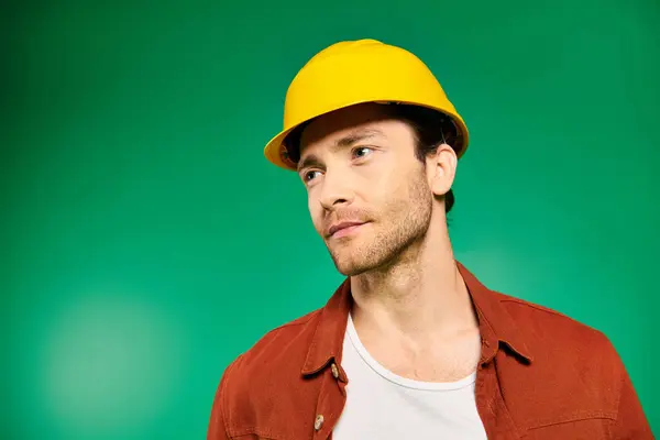 Handsome worker in uniform and hard hat stands confidently against vivid green background. — Stock Photo