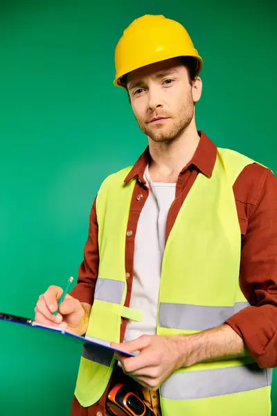 Un hombre con un chaleco de seguridad amarillo escrito en un portapapeles. - foto de stock