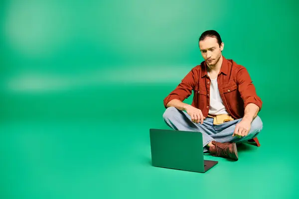 A man in a uniform sits on the floor working on a laptop. — Stock Photo