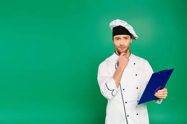 Bello chef maschio in uniforme bianca che tiene un appunti su sfondo verde. — Foto stock