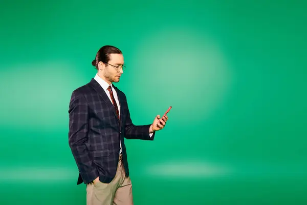 Un hombre de negocios guapo con un traje elegante sosteniendo un teléfono celular frente a una pantalla verde. - foto de stock