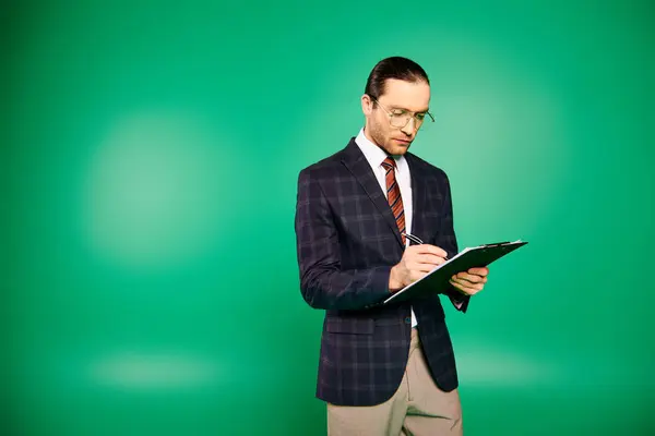 Bonito homem de negócios em um terno chique e gravata, segurando uma área de transferência em um pano de fundo verde. — Fotografia de Stock
