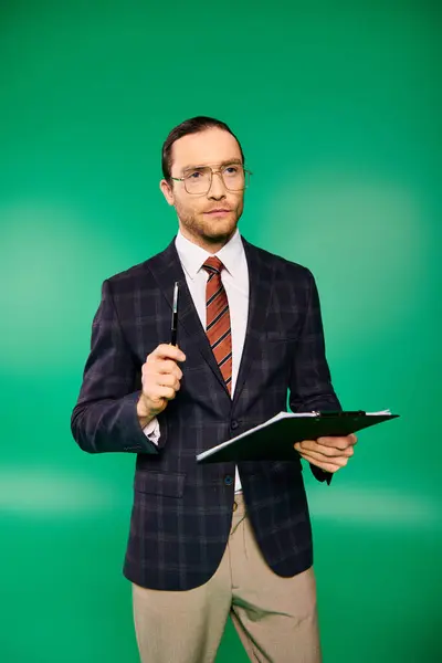 Handsome businessman in chic suit holding a clipboard on green backdrop. — Stock Photo