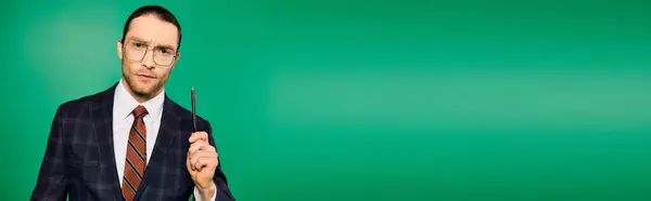 Ein stilvoller Geschäftsmann im schicken Anzug mit Stift vor grünem Hintergrund. — Stockfoto