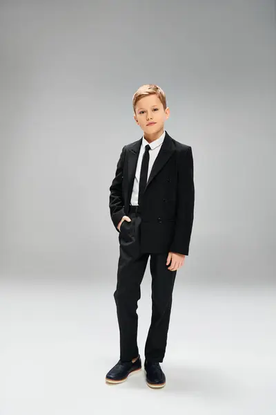 Un ragazzo preadolescente in giacca e cravatta in piedi su uno sfondo grigio. — Foto stock