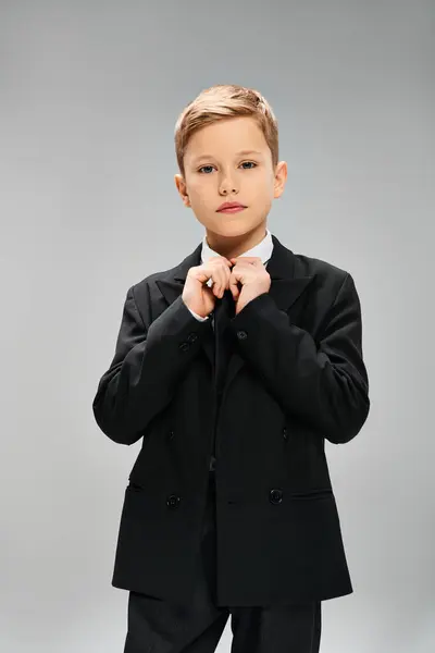 Un niño preadolescente en traje elegante y corbata contra un fondo gris. - foto de stock