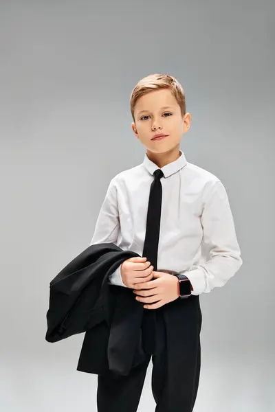 Красивый молодой мальчик одет в белую рубашку и черный галстук, излучая элегантность на сером фоне. — стоковое фото