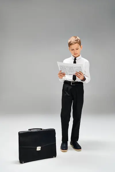Little boy stands next to suitcase on gray backdrop. — Stock Photo