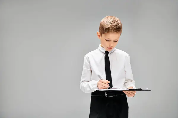 Preadolescent boy in white shirt and tie, focused on writing notes on clipboard. — Stock Photo