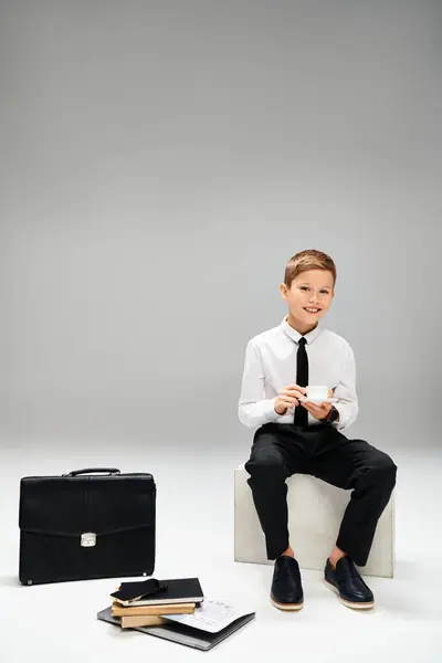 A young boy in smart attire sits beside a briefcase. — Stock Photo