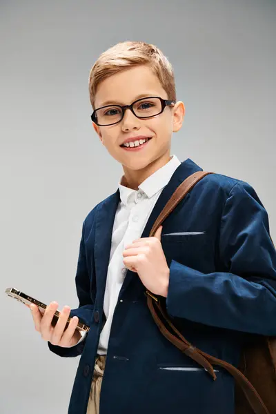 Young boy in glasses, holding cellphone. Business concept on gray backdrop. — Stock Photo