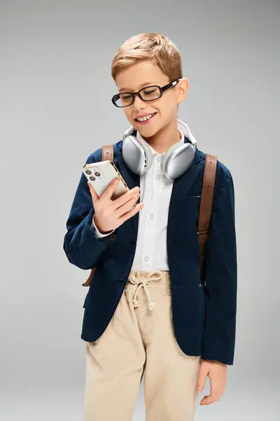 A stylish preadolescent boy in elegant attire, wearing headphones and holding a cell phone. — Stock Photo