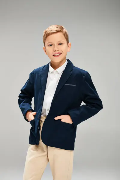 A young boy dressed in a stylish blue jacket and tan pants, exuding elegance on a gray backdrop. — Stock Photo