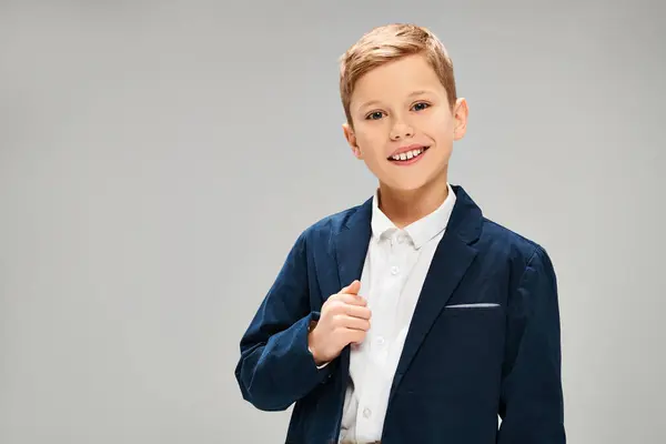 Ein kleiner vorpubertärer Junge in blauer Jacke und weißem Hemd, der vor grauem Hintergrund Eleganz und Raffinesse ausstrahlt.. — Stockfoto