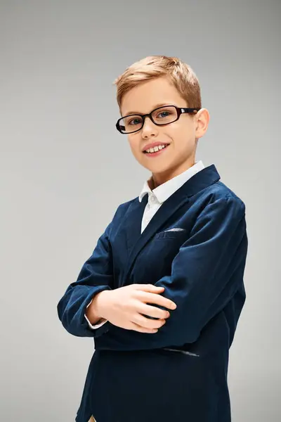 Um menino pré-adolescente em traje elegante, vestindo óculos, bate uma pose confiante contra um pano de fundo cinza. — Fotografia de Stock