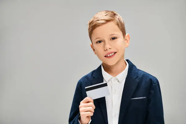 Preadolescent boy in a sharp suit confidently holds a credit card. — Stock Photo