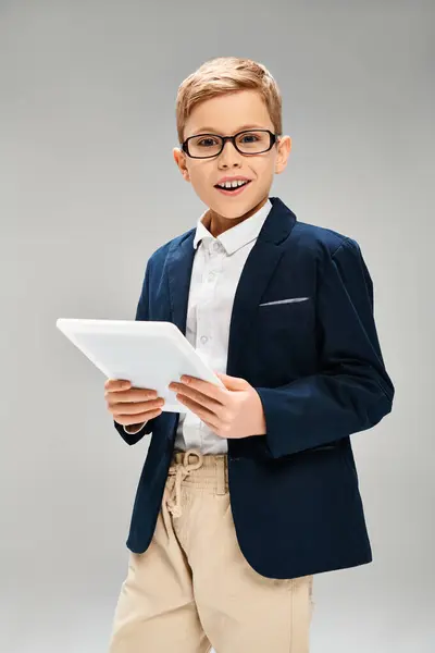 A preadolescent boy in a suit and glasses confidently holds a tablet. — Stock Photo