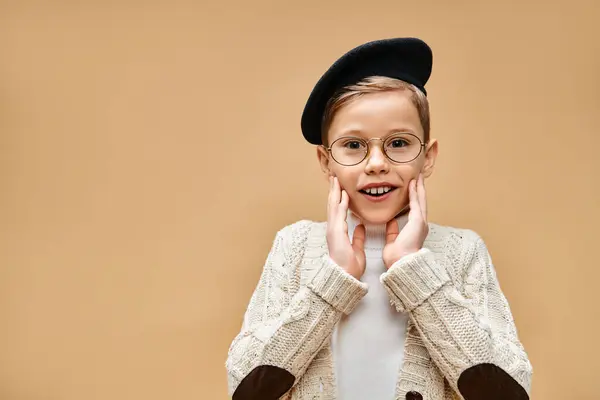 Молодий хлопчик в окулярах і капелюсі, одягнений як кінорежисер, на тлі бежевого фону. — стокове фото