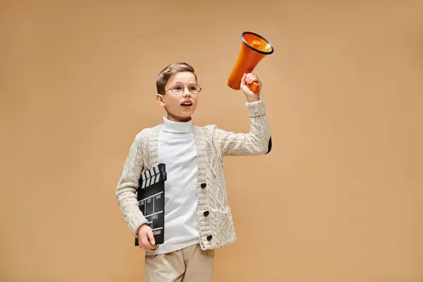 Um jovem rapaz, vestido de realizador de cinema, tem um megafone e um aplauso.. — Fotografia de Stock