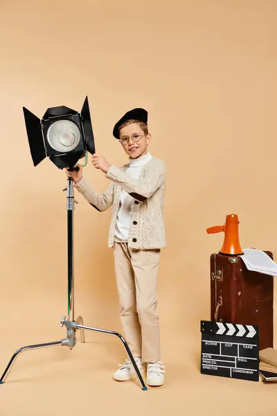 A cute preadolescent boy dressed as a film director poses with a light in hand on a beige backdrop. — Stock Photo