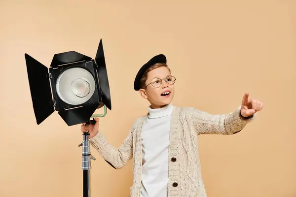 A cute preadolescent boy dressed as a film director, holding a camera and a light. — Stock Photo